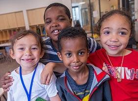 Four young students smile for a photo in a classroom.